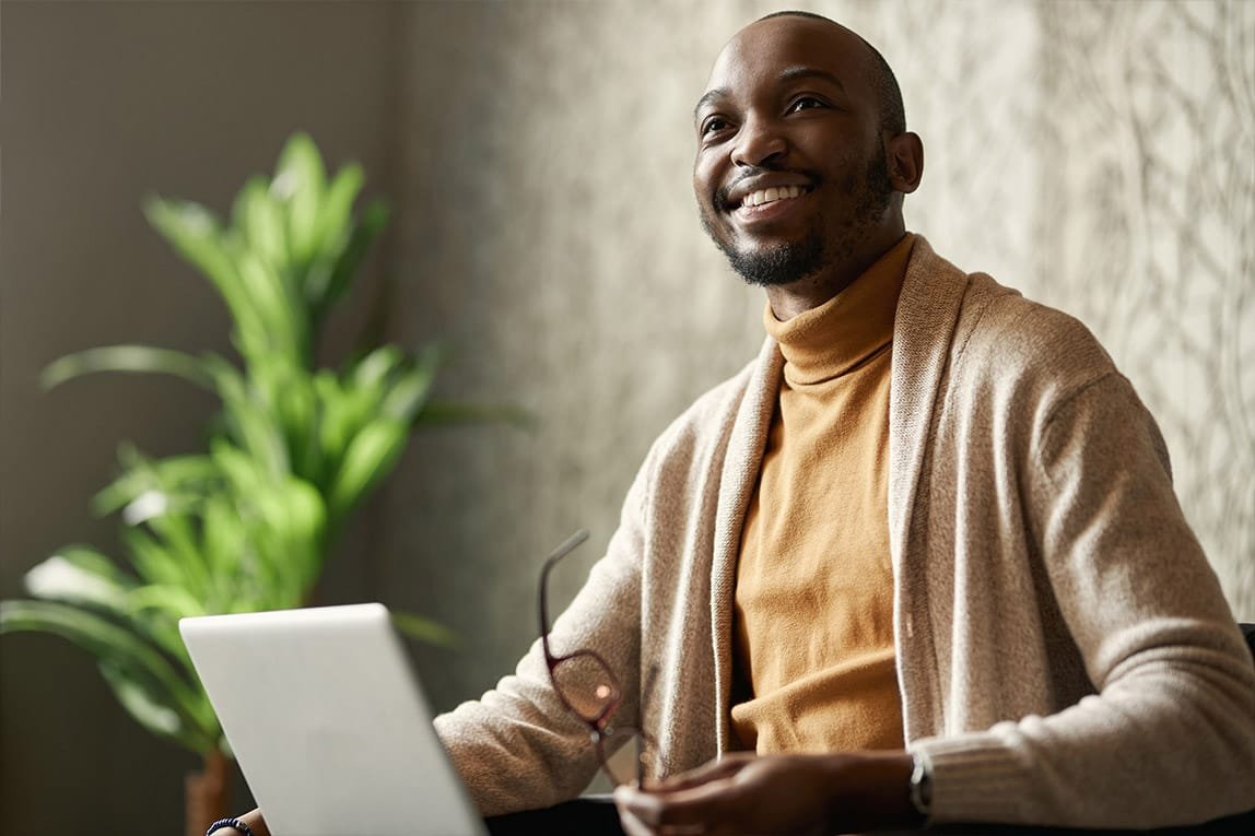 Man smiling, looking up from his computer while holding his glasses